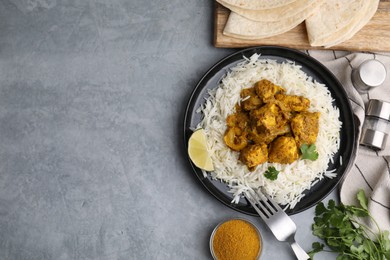 Photo of Delicious chicken curry with rice and ingredients on grey table, flat lay. Space for text