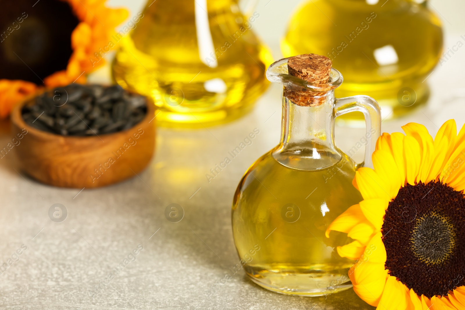 Photo of Sunflower cooking oil, seeds and yellow flower on light grey table, closeup. Space for text