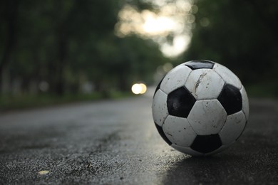 Photo of Dirty leather soccer ball on wet road, space for text