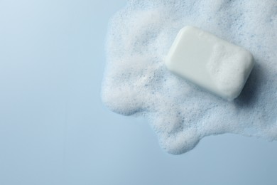 Photo of Soap with fluffy foam on light blue background, top view. Space for text