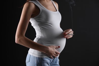 Photo of Pregnant woman smoking cigarette on black background, closeup. Space for text