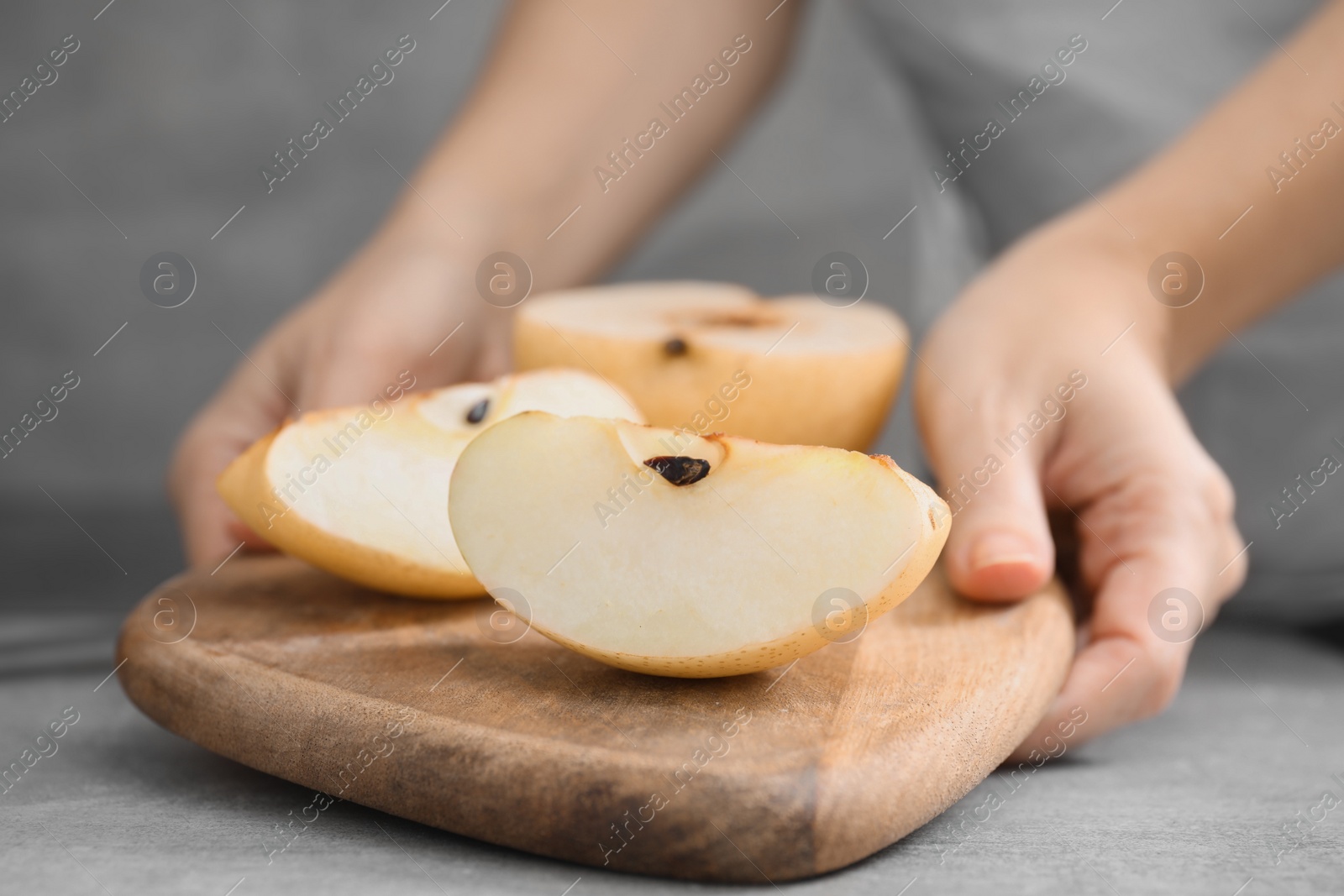 Photo of Woman holding board with fresh cut apple pears at grey table, closeup