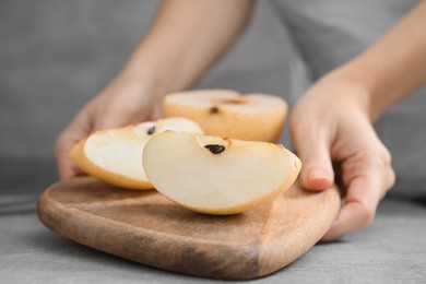 Woman holding board with fresh cut apple pears at grey table, closeup