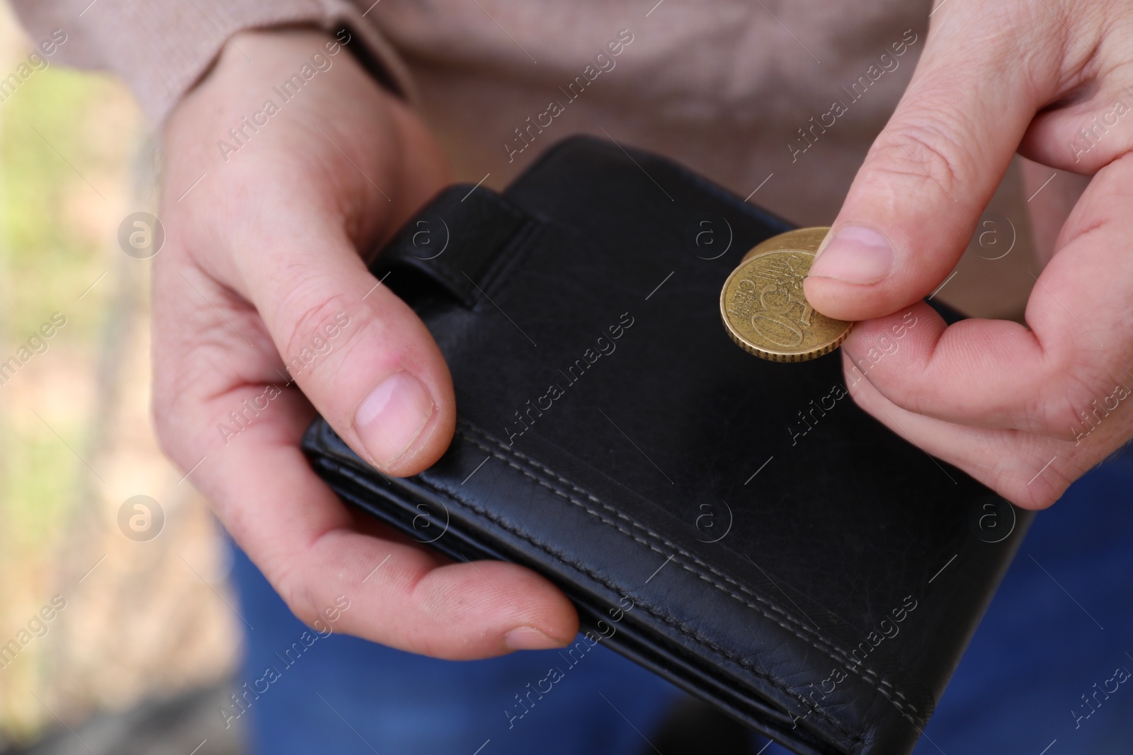 Photo of Poor man holding coins and empty wallet outdoors, closeup