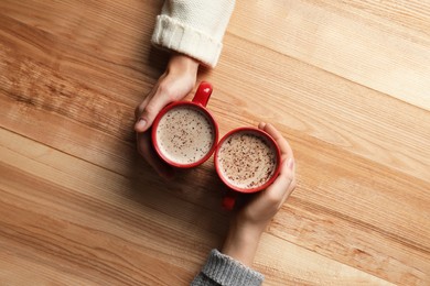 Photo of Women with cups of coffee at wooden table, top view