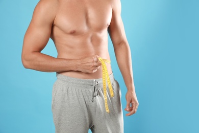 Photo of Young man with slim body using measuring tape on light blue background, closeup view. Space for text