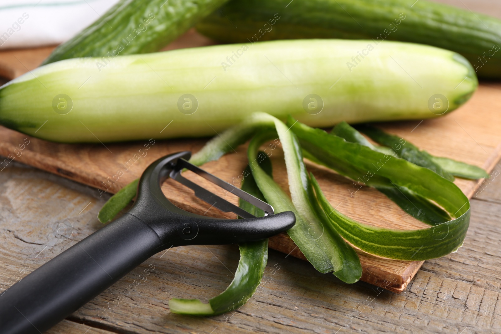 Photo of Fresh cucumbers, peels and peeler on wooden table, closeup