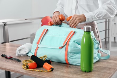 Photo of Businesswoman packing sports stuff for training into bag in office, closeup