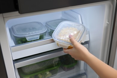 Photo of Woman putting container with tasty corn kernels into fridge, closeup. Food storage