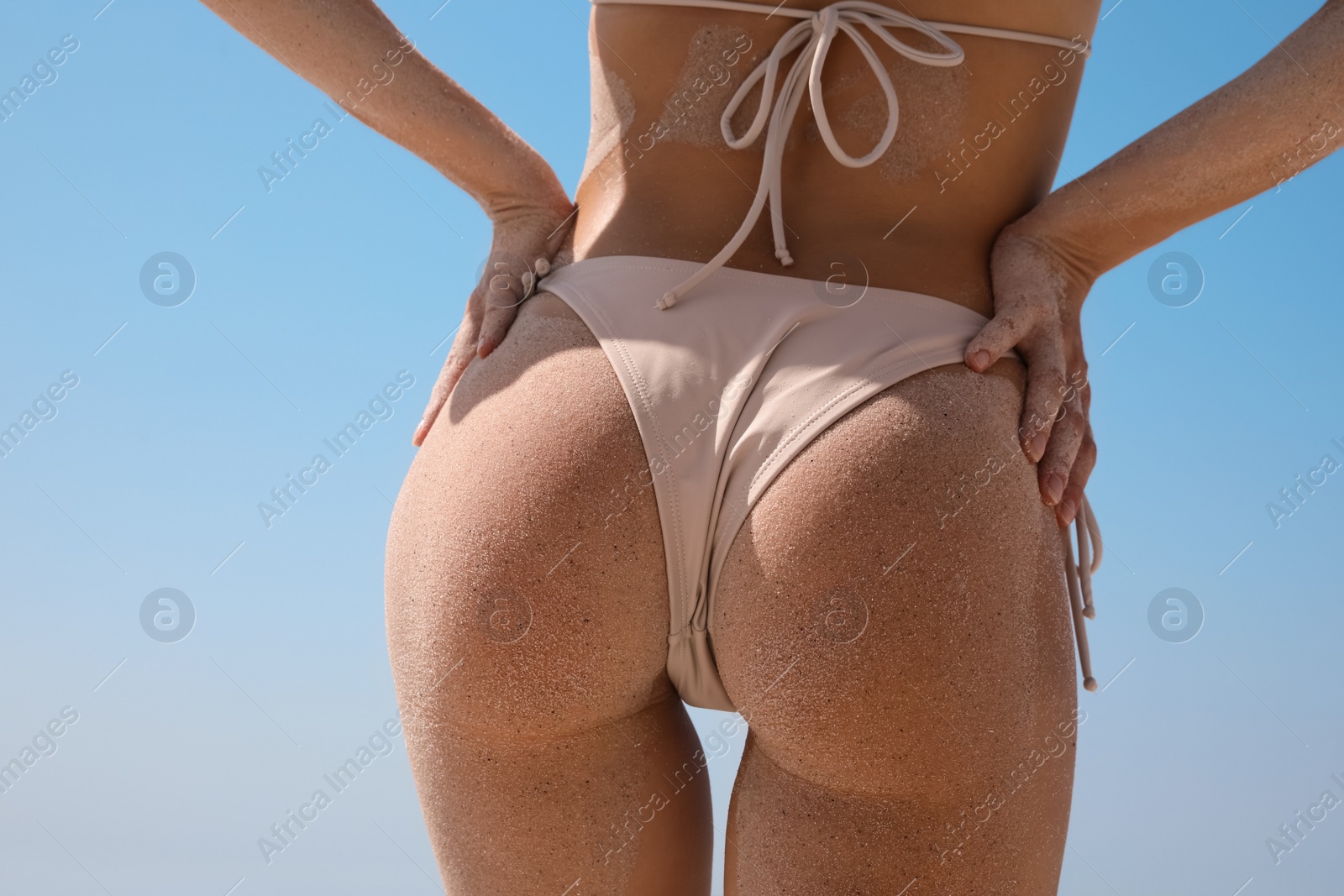 Photo of Woman with sand on perfect body in bikini against blue sky, closeup. Back view