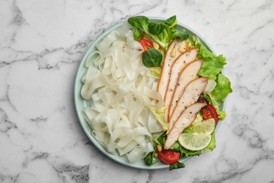 Photo of Tasty cooked rice noodles with chicken and vegetables on white marble table, top view