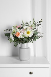 Bouquet with beautiful flowers on white chest of drawers indoors