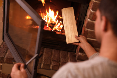 Photo of Man putting dry firewood into fireplace at home, closeup. Winter vacation