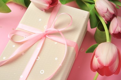 Photo of Beautiful gift box with bow, tulips and confetti on pink background, closeup