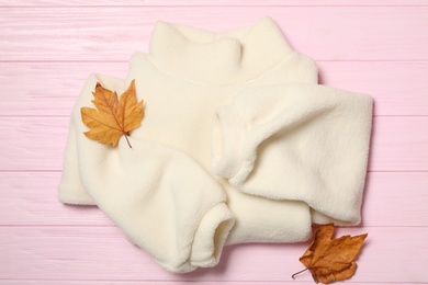 Photo of Warm sweater and dry leaves on pink wooden background, flat lay. Autumn season