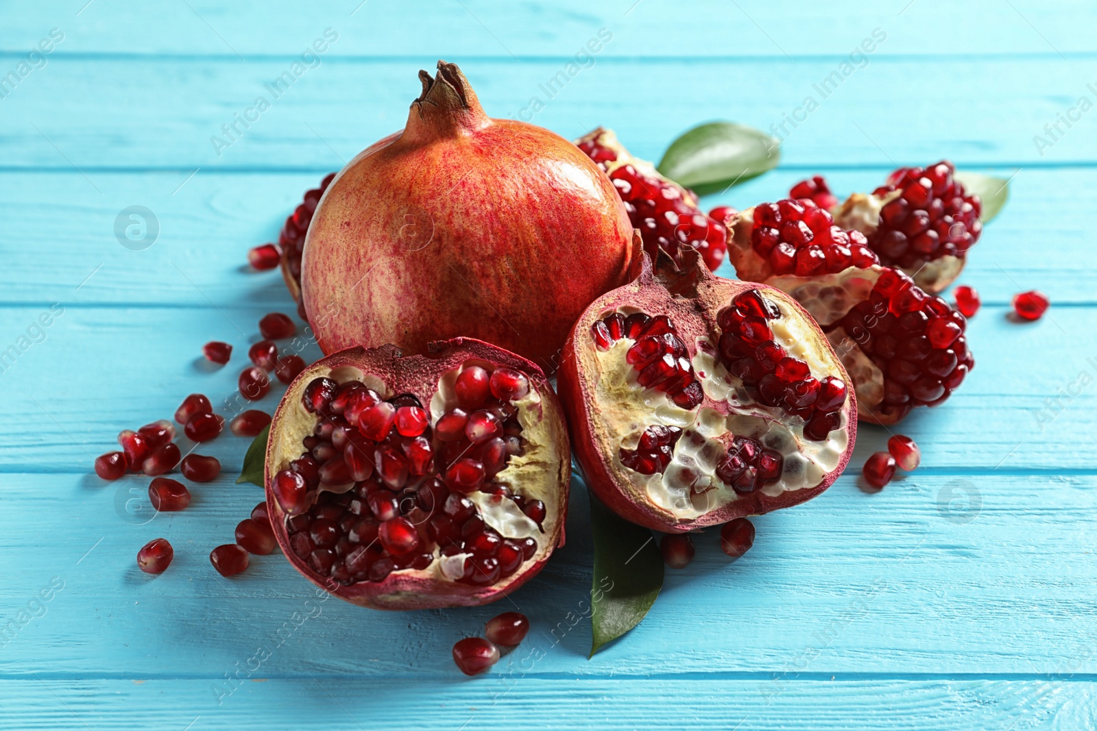 Photo of Ripe pomegranates and leaves on color wooden background