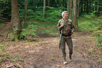 Photo of Man with hunting rifle and binoculars wearing camouflage in forest. Space for text