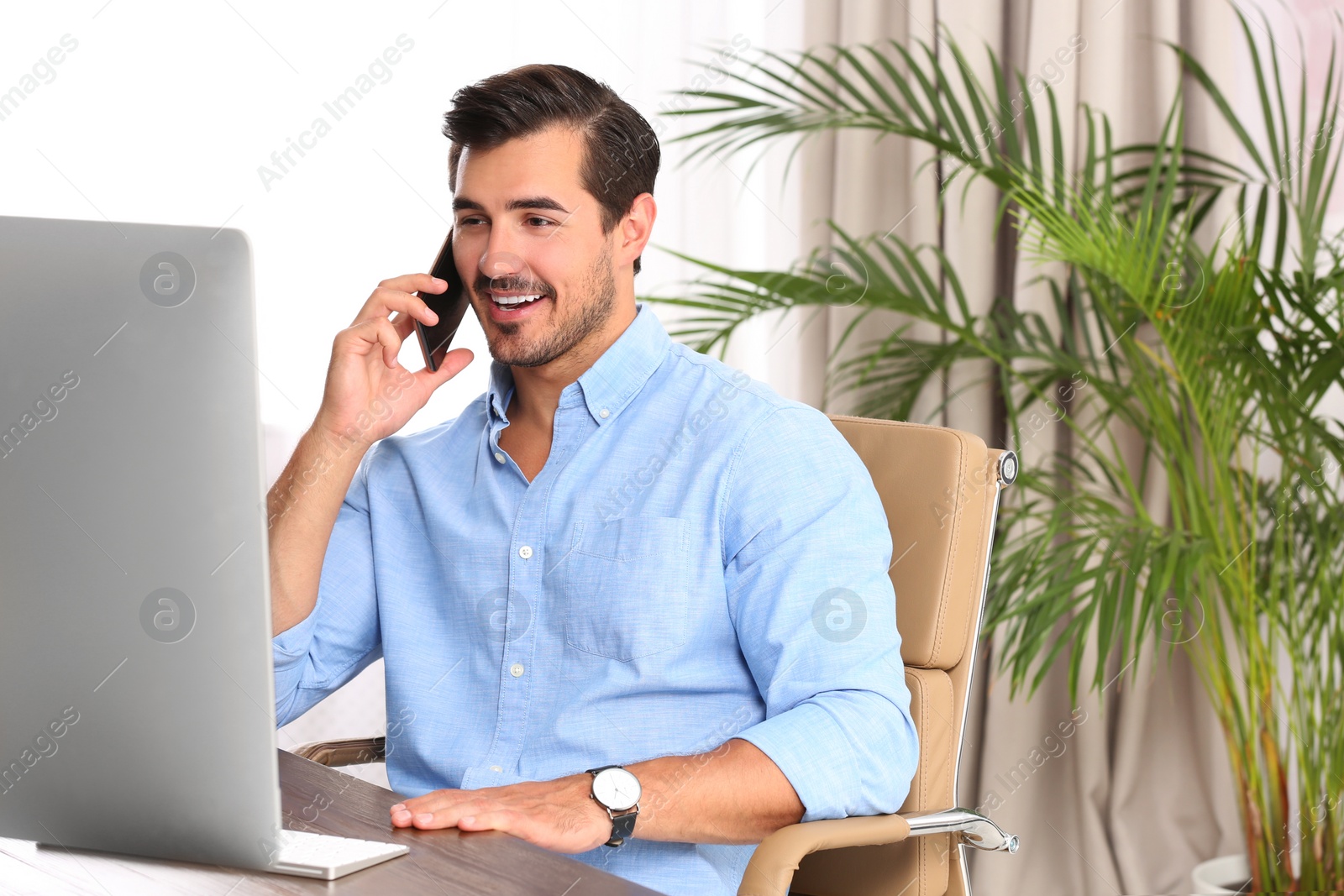 Photo of Handsome young man working with smartphone and computer at table in office