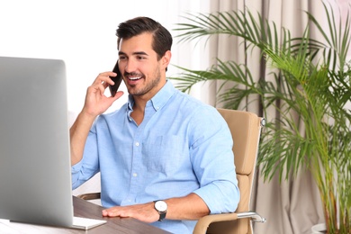 Handsome young man working with smartphone and computer at table in office