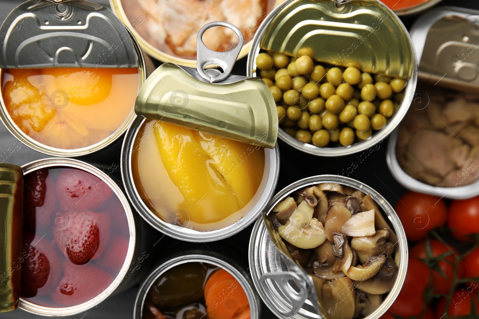 Photo of Open tin cans with different products as background, top view