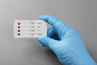 Photo of Doctor holding disposable multi-infection express test on light grey background, closeup