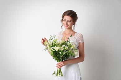 Photo of Young bride wearing wedding dress with beautiful bouquet on light background
