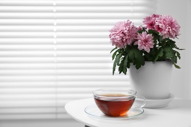 Beautiful chrysanthemum plant in flower pot and cup of tea on white table indoors, space for text