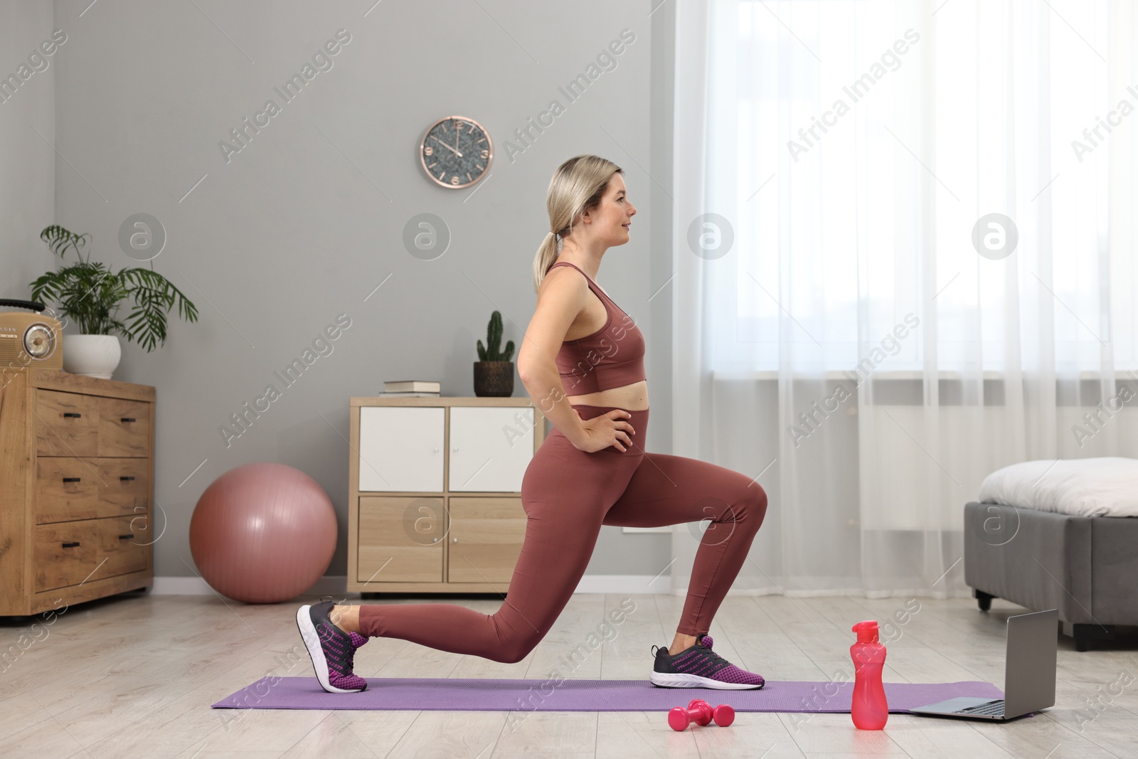 Photo of Online fitness trainer. Woman doing exercise near laptop at home