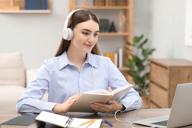 Photo of E-learning. Young woman with book during online lesson at table indoors