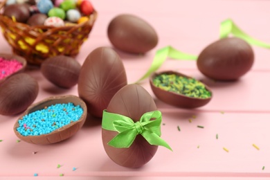Photo of Sweet chocolate eggs and sprinkles on pink wooden table