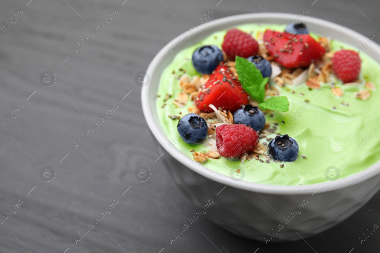 Photo of Tasty matcha smoothie bowl served with berries and oatmeal on grey wooden table, closeup with space for text. Healthy breakfast