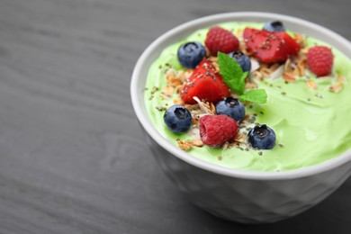 Photo of Tasty matcha smoothie bowl served with berries and oatmeal on grey wooden table, closeup with space for text. Healthy breakfast