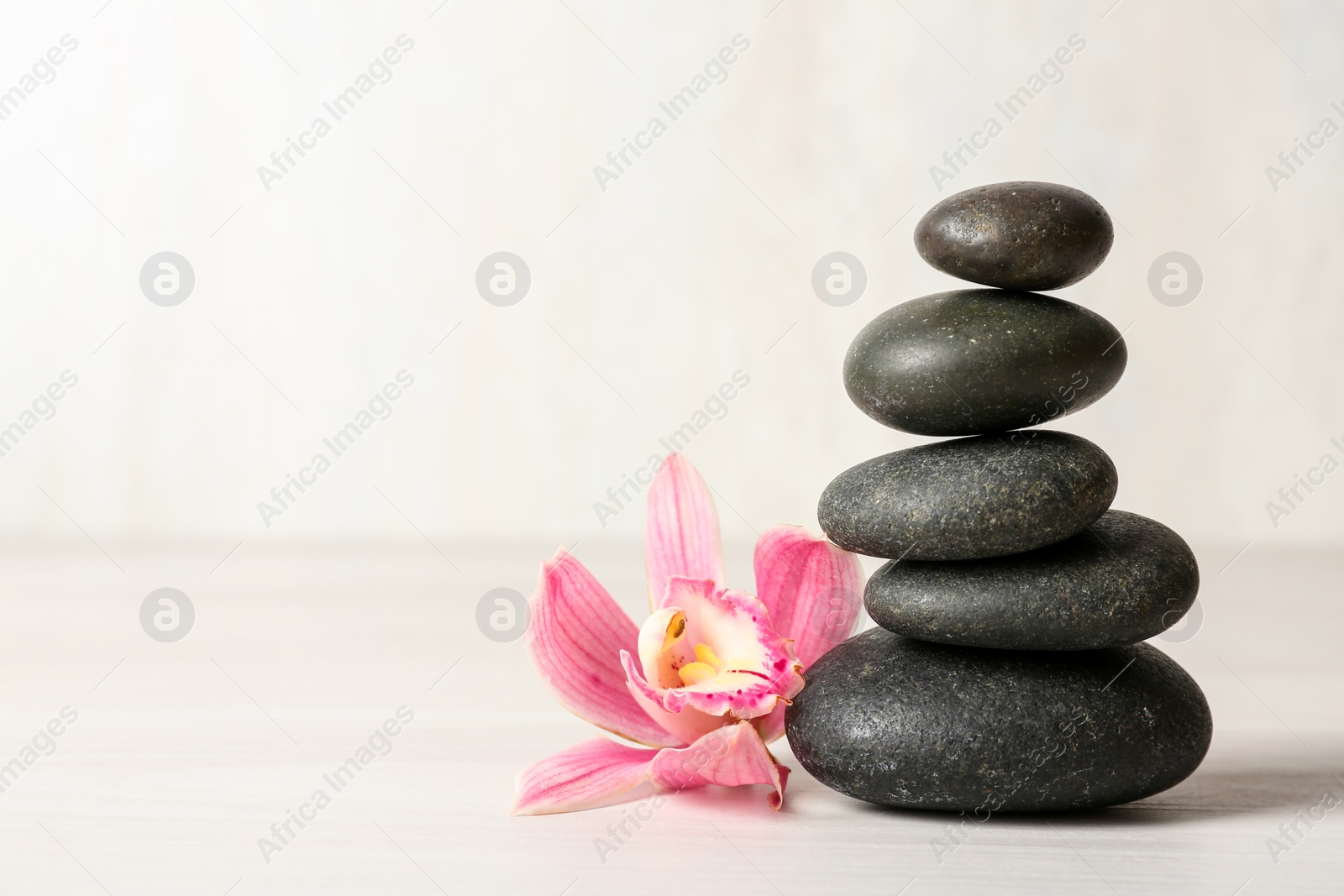 Photo of Stack of spa stones and flower on table against white background, space for text