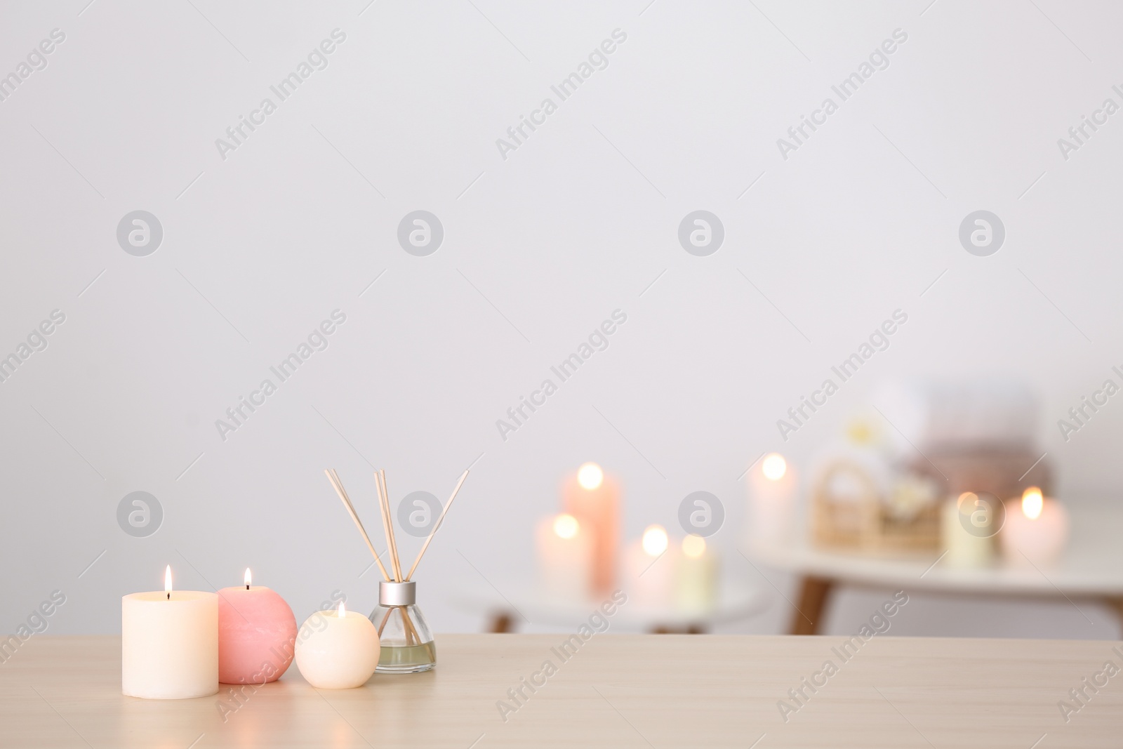 Photo of Candles and reed air freshener on table against blurred background, space for text. Spa concept