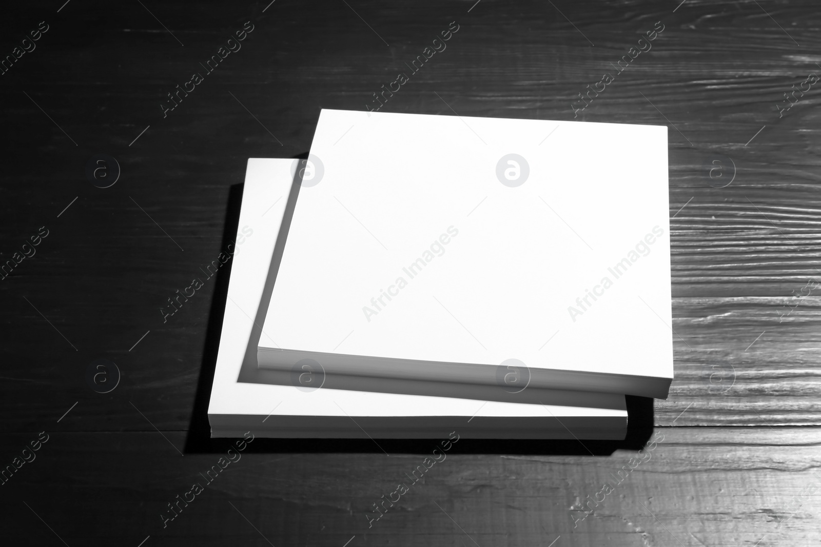 Photo of Stack of blank paper sheets for brochure on black wooden background. Mock up