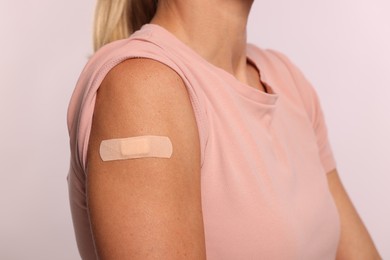 Woman with adhesive bandage on arm after vaccination on light background, closeup