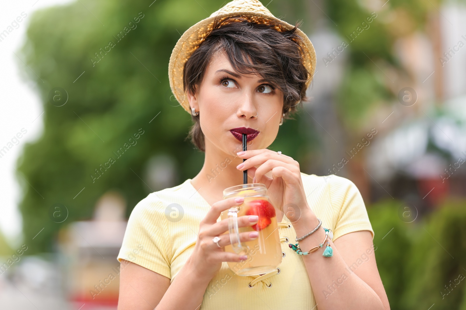 Photo of Young woman with mason jar of tasty lemonade outdoors