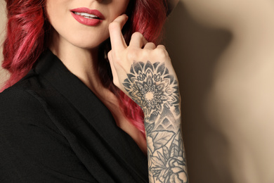 Photo of Beautiful woman with tattoos on arm against beige background, closeup