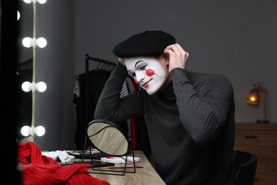 Photo of Mime artist putting on beret near mirror in dressing room
