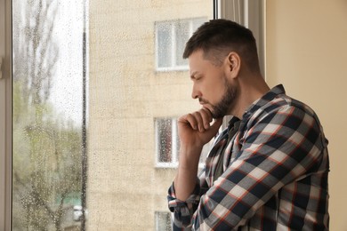 Photo of Depressed man near window at home. Space for text