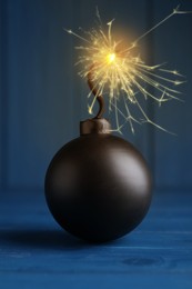 Image of Old fashioned black bomb with lit fuse on blue wooden table