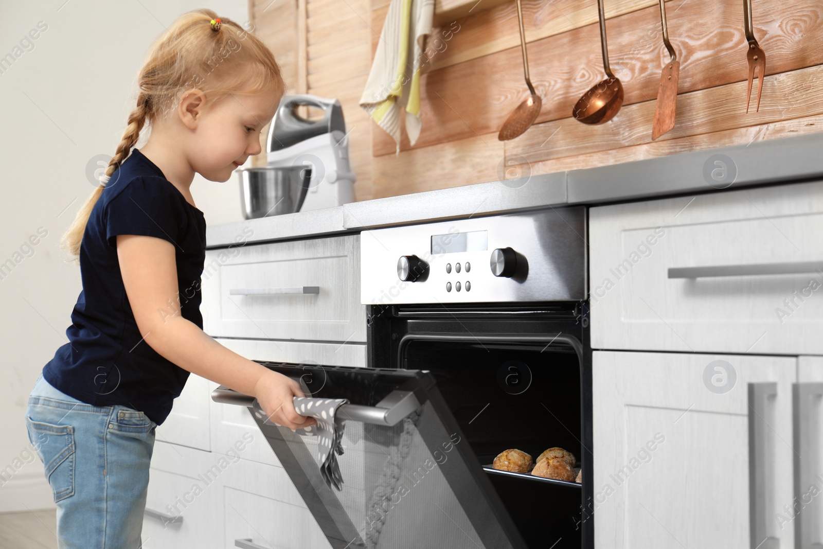 Photo of Little girl checking cookies in oven at home