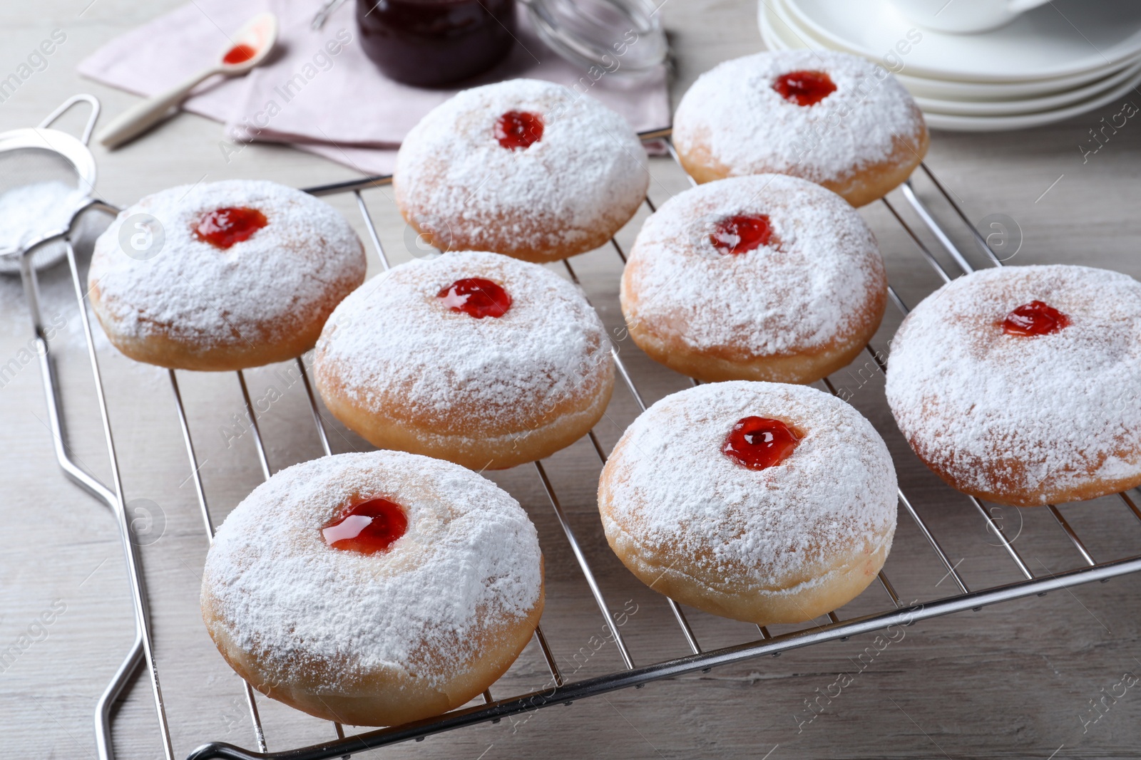 Photo of Many delicious donuts with jelly and powdered sugar on cooling rack