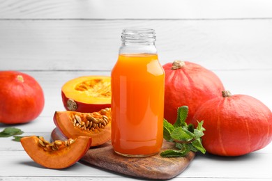 Photo of Tasty pumpkin juice in glass bottle and pumpkins on white wooden table