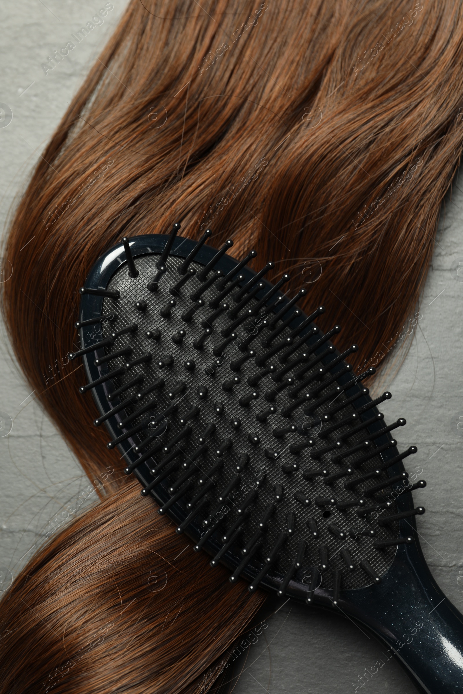 Photo of Stylish brush with brown hair strand on dark grey table, top view