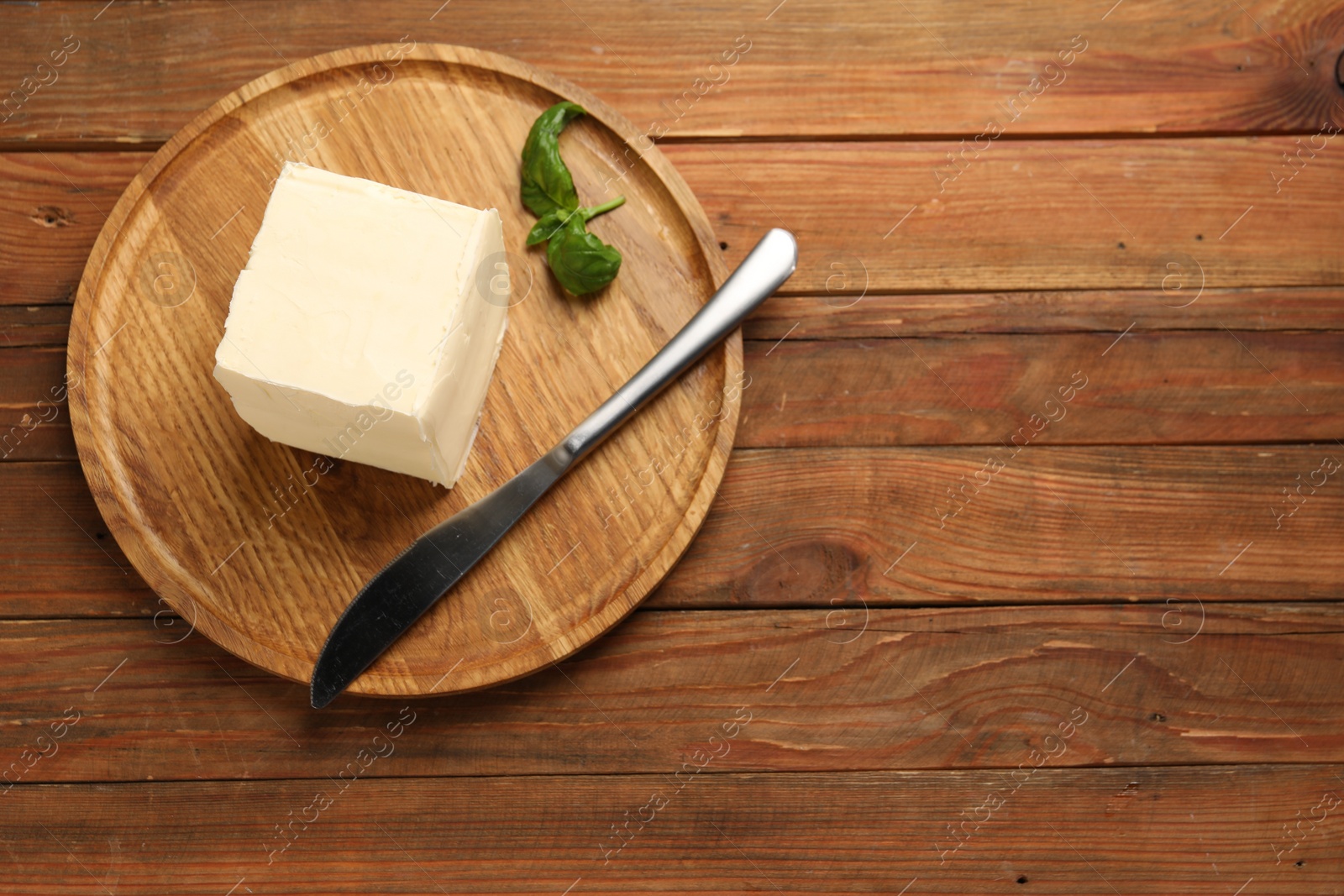 Photo of Block of tasty butter, knife and basil on wooden table, top view. Space for text