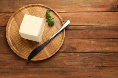 Block of tasty butter, knife and basil on wooden table, top view. Space for text