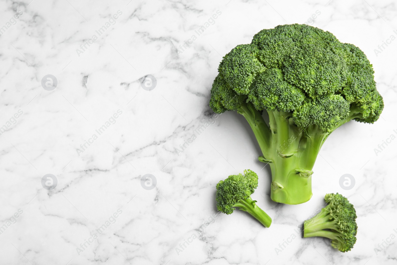 Photo of Fresh green broccoli on white marble table, flat lay. Space for text