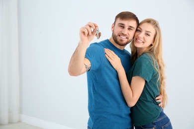Photo of Happy young couple with key from their new house indoors, space for text