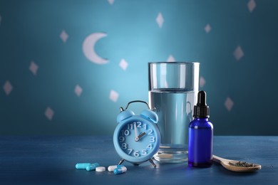 Photo of Alarm clock and different remedies for insomnia treatment near glass of water on table against blue wall decorated with stars and crescent